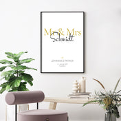 Mr & Mrs in Gold. Poster mit Personalisierten Nachnahmen, Vornamen, Ort und Datum. Bild im schwarzen Bilderrahmen an der Wand.