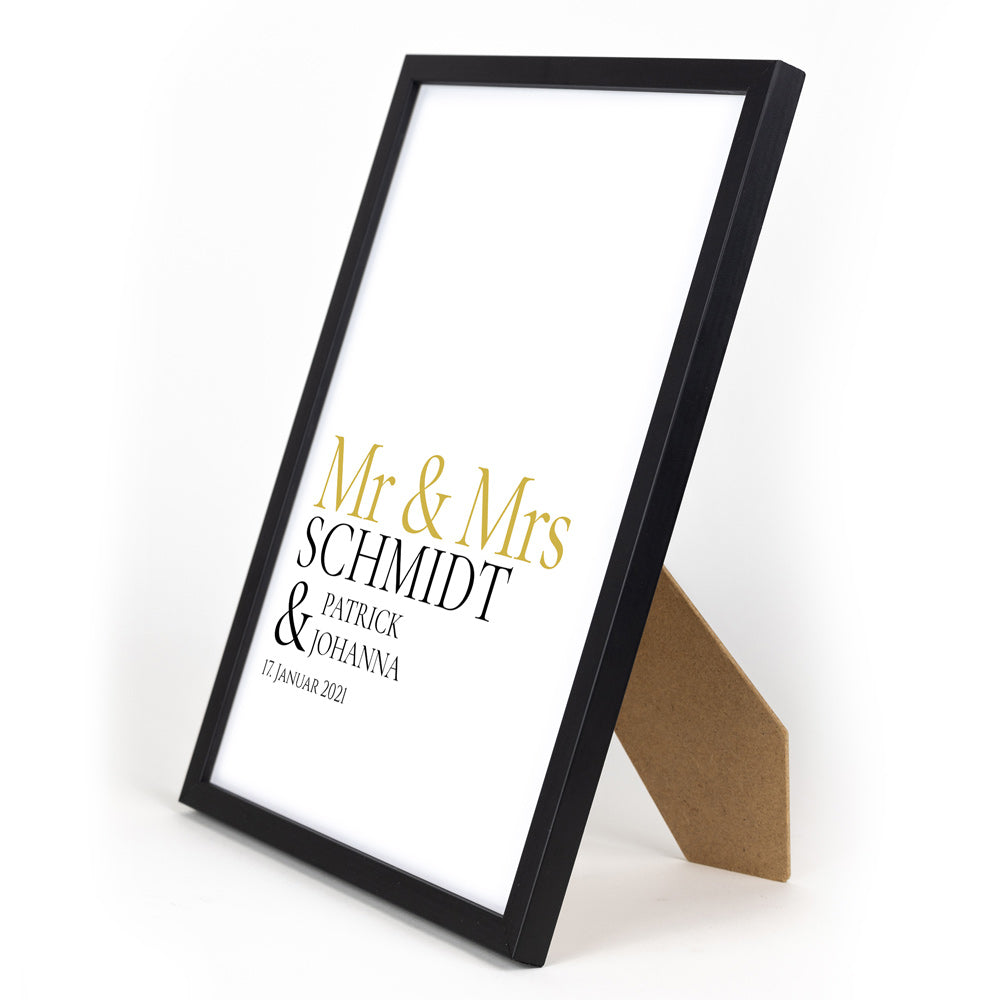 Mr & Mrs in goldener Schrift, darunter personalisierbarer Familienname, Vornamen und Datum. Bild im schwarzen Din A4 Bilderrahmen.