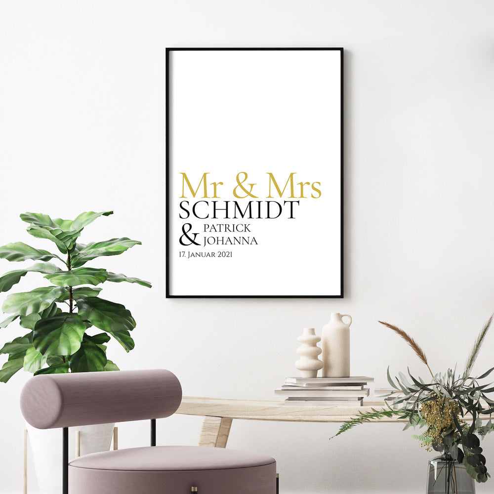Mr & Mrs in goldener Schrift, darunter personalisierbarer Familienname, Vornamen und Datum. Bild im schwarzen Bilderrahmen an der Wand.