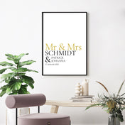 Mr & Mrs in goldener Schrift, darunter personalisierbarer Familienname, Vornamen und Datum. Bild im schwarzen Bilderrahmen an der Wand.