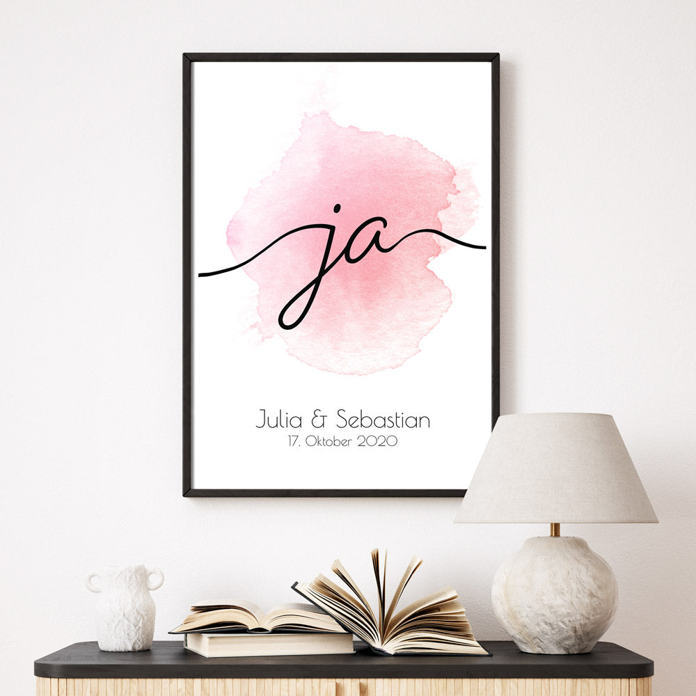 Ja Schriftzug, rosa Hintergrund auf weißem Grund. Unten personalisierte Vornamen & Datum. Bild im Rahmen an der Wand.