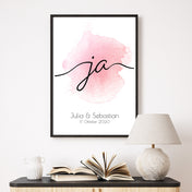 Ja Schriftzug, rosa Hintergrund auf weißem Grund. Unten personalisierte Vornamen & Datum. Bild im Rahmen an der Wand.