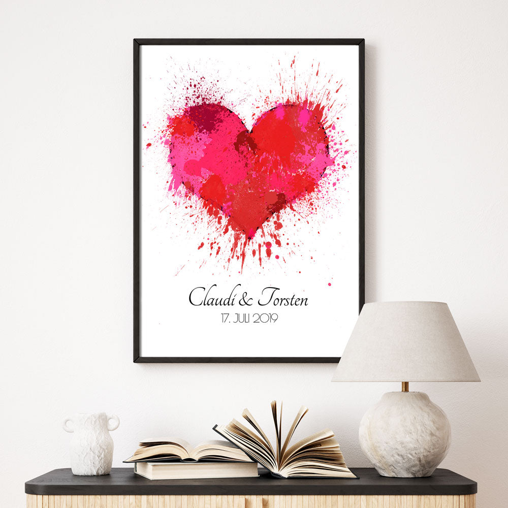 Rotes Herz Poster mit personalisierten Namen und Datum darunter. Bild im schwarzem Bilderrahmen an der Wand über einer Kommode.