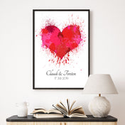 Rotes Herz Poster mit personalisierten Namen und Datum darunter. Bild im schwarzem Bilderrahmen an der Wand über einer Kommode.