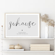 Personalisiertes Poster im Regal im Holzbilderrahmen. Zuhause Schriftzug auf grauem Hintergrund. Individuelle Koordinaten und Vornamen darunter.
