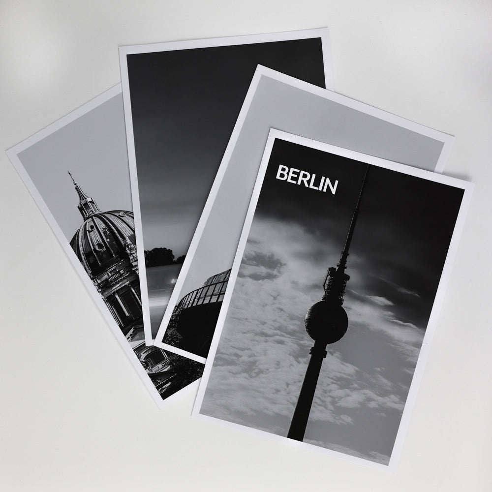 4er Berlin Poster Set in schwarz Weiß vom Fernsehturm, Berliner Dom, Siegessäule und einer BVG U-Bahn. Poster liegen übereinander auf einem Tisch.