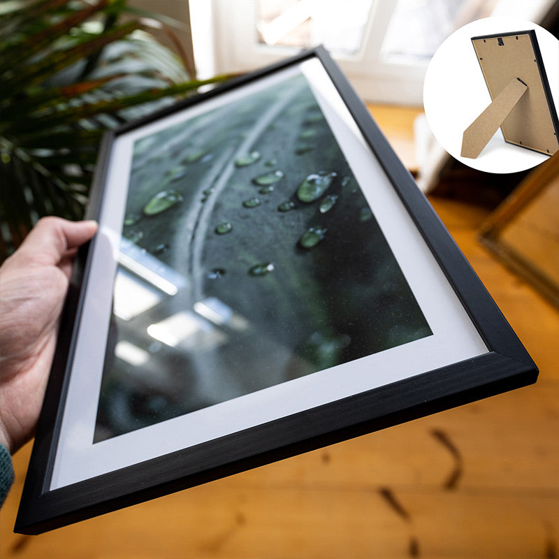 Natur Poster von Regentropfen auf einem Blatt im Bilderrahmen.  Schwarzer Rahmen mit Aufsteller für Din A4 gehalten in der Hand.