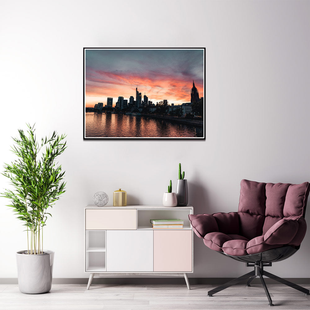 Frankfurt Skyline Poster im Querformat. Roter Himmel zum Sonnenuntergang, Spiegelung im Main.  Bild im schwarzen Rahm an der Wand im Wohnzimmer.