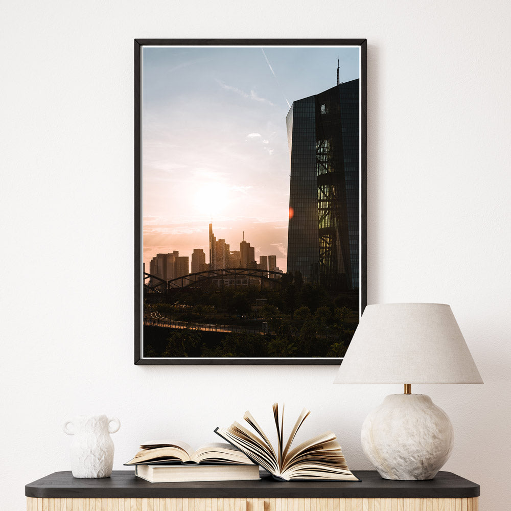 Frankfurt Poster der EZB zum Sonnenuntergang. Im Hintergrund die Frankfurt Skyline. Bild im schwarzen Bilderrahmen über einer Kommode.