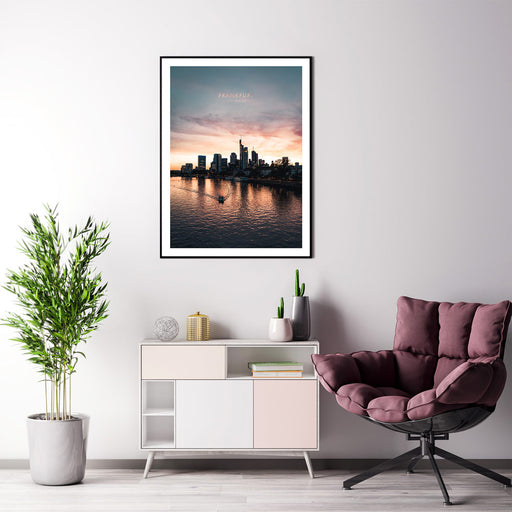 Frankfurt am Main Skyline Poster. Farbenfroher Sonnenuntergang, kleines Boot fährt im Vordergrund über den Main. Bild mit weißen umlaufenden Rand. Bild gerahmt an der Wohnzimmer Wand.