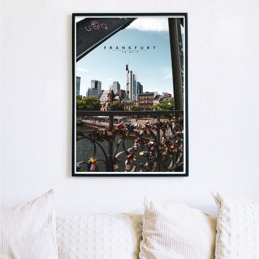 Frankfurt Poster im retro look der Frankfurter Skyline und im Vordergrund Liebesschlösser. Poster gerahmt im schwarzen Bilderrahmen an der Wand über einem hellen Sofa.