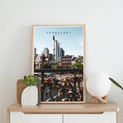 Frankfurt Poster im retro look der Frankfurter Skyline und im Vordergrund Liebesschlösser. Bild im hellen Rahmen auf einer Kommode stehend.