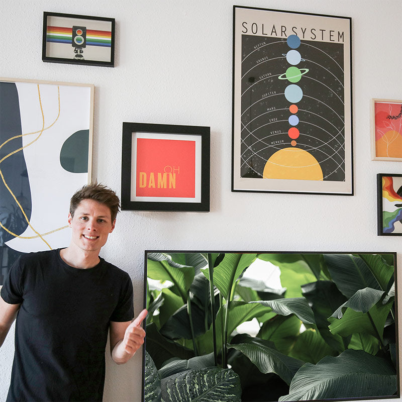 Gründer von 4one Pictures, Kilian Dalchow vor einer Wohnzimmer Bilderwand mit farbenfrohen Postern und dem 4one Pictures Bilderrahmen