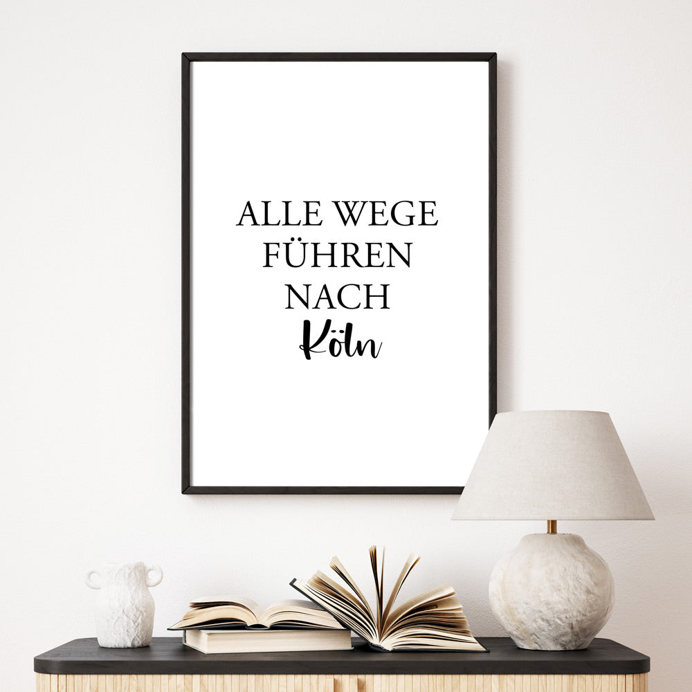 Alle Wege führen nach Köln Poster. Spruch Bild mit schwarzer Schrift auf Weißem Papier. Poster im schwarzen Bilderrahmen an der Wand im Flur.