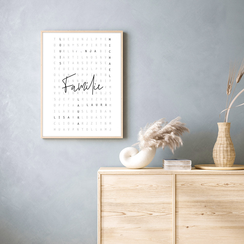 Personalisierbares Poster im beigen Bilderrahmen an einer grauen Wand. Vornamen sind im Kreuzworträtsel Design eingefügt, in der Mitte steht Familie.