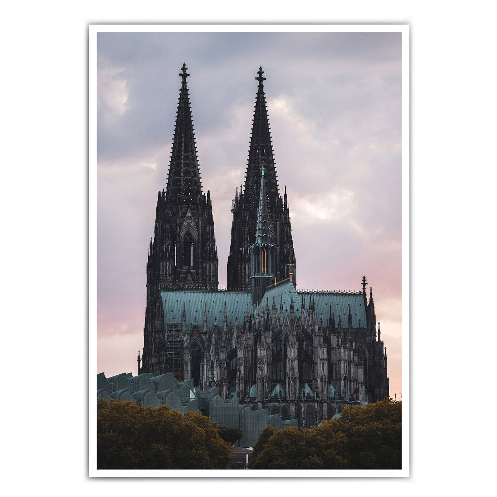 Kölner Dom Poster im Sonnenuntergang mit rötlichem Himmel. Im Vordergrund das Museum Ludwig und Bäume. 