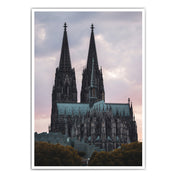 Kölner Dom Poster im Sonnenuntergang mit rötlichem Himmel. Im Vordergrund das Museum Ludwig und Bäume. 