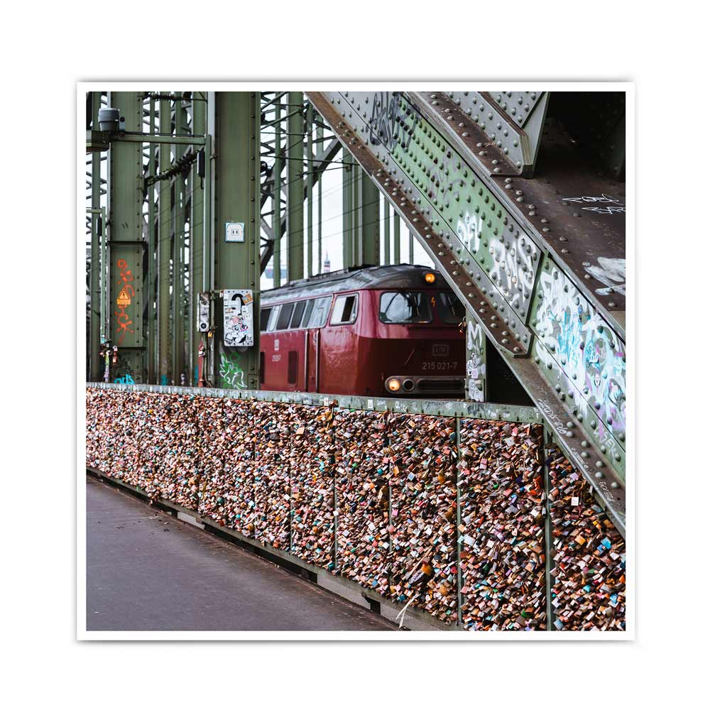 Bild mit Köln Motiv im quadratischen Format. Bahn fährt über die Hohenzollernbrücke, im Vordergrund sind die Liebesschlösser. Industrie Look.