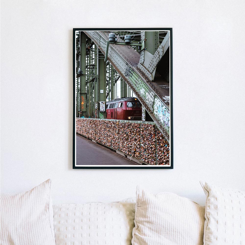 Bild mit Köln Motiv im Bilderrahmen über dem Sofa. Bahn fährt über die Hohenzollernbrücke, im Vordergrund sind die Liebesschlösser. Industrie Look.