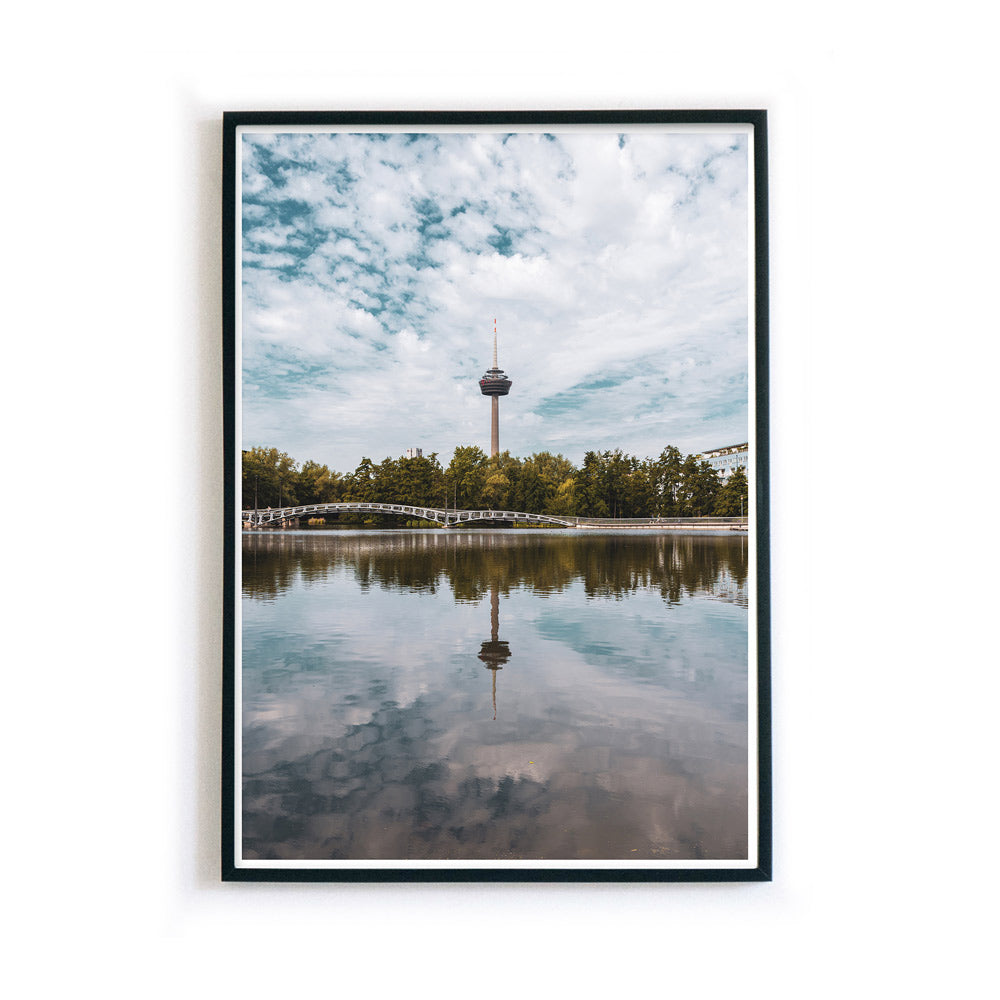 Sommer Köln Bild im Bilderrahmen in Hochformat. Fernsehturm ist mittig im Bild und spiegelt sich im See im Vordergrund.