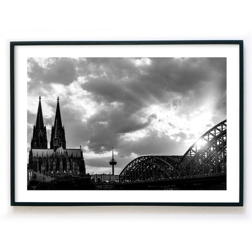 Schwarz Weiß Köln Poster im Querformat. Sonnenuntergang bei wolkigen Himmel über dem Kölner Dom, Hohenzollernbrücke oder dem Fernsehturm. Bild fertig gerahmt mit weißen Rand.
