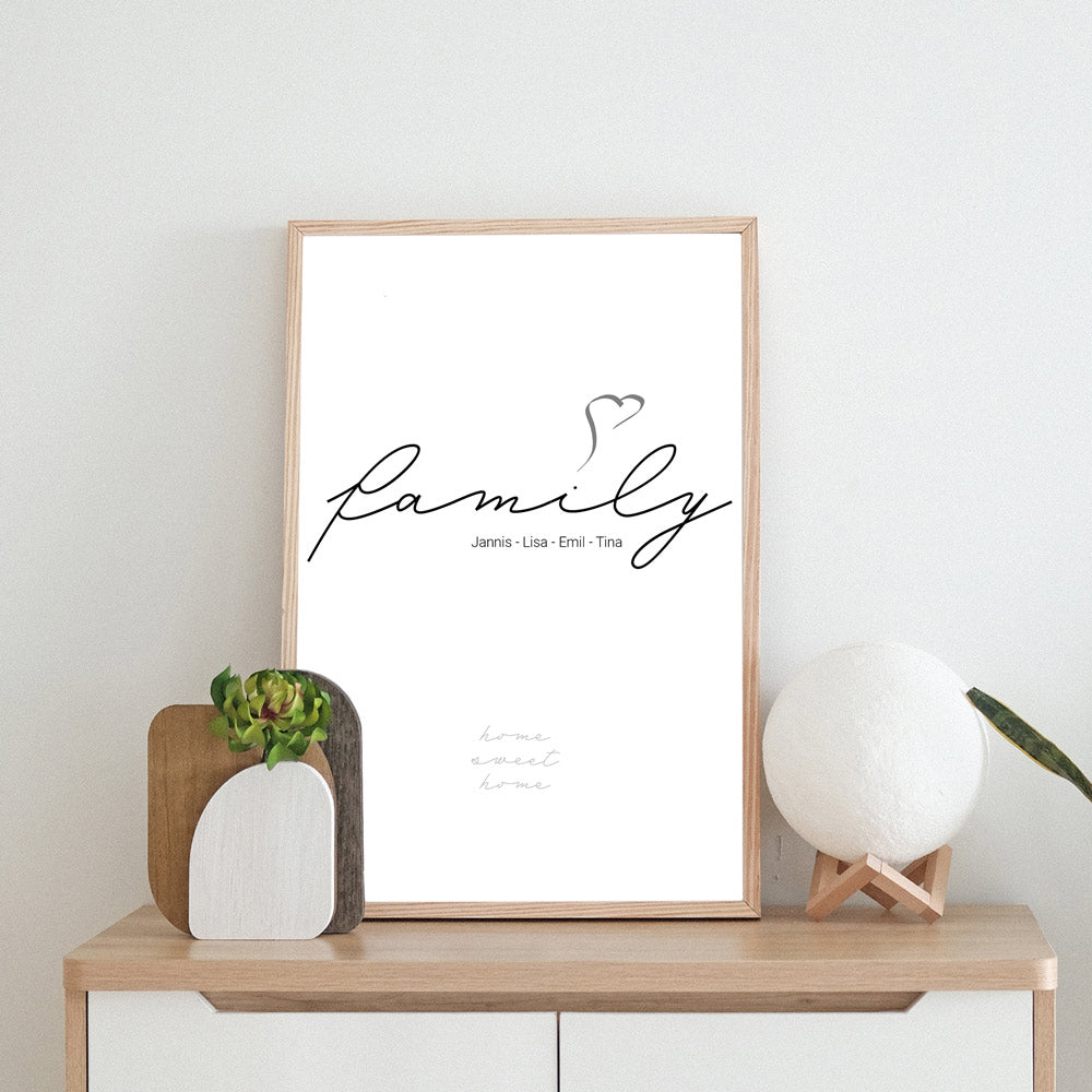 family mit herz über dem i. Personalisierte Vornamen unter Family. Darunter der Spruch Home Sweet Home. Im beigen Rahmen auf einer Kommode.