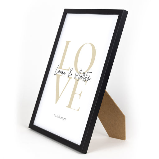 Personalisiertes Love Poster. Beige Love auf weißem Papier, individuelle Vornamen in der Mitte und Datum darunter. Bild im Din A4 Rahmen mit Aufsteller.